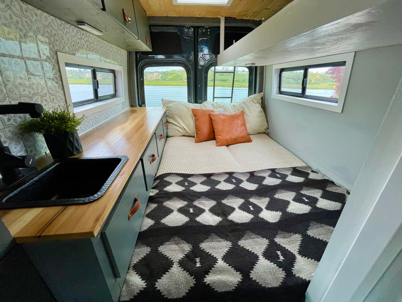 This cozy RV rental features a full bed, built-in kitchen counter with a sink, and scenic window views of the outdoors. — photo 5