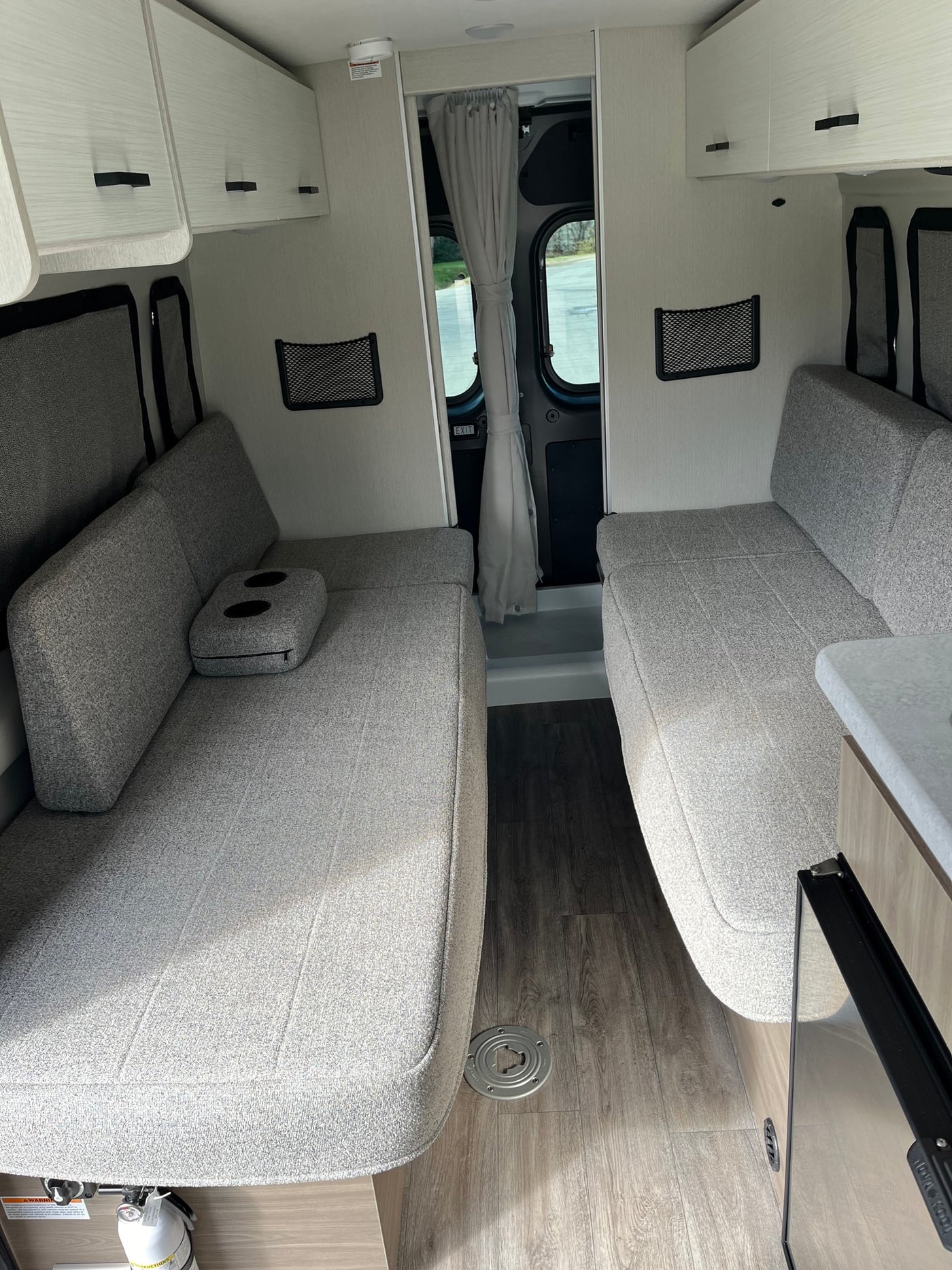 Bright RV rental interior with comfortable facing grey sofas, overhead cabinets, and wood-look flooring. Perfect for travel! — photo 16