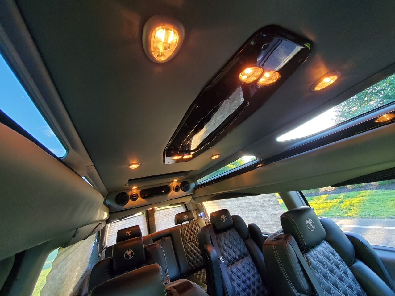 Experience a luxury RV rental's interior! Plush black quilted leather seats, bright ambient lighting, & large windows fill this custom van.