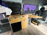 Bright RV rental camper van interior: compact kitchen with sink, Dometic fridge, bamboo cabinetry, and bed area for travel.