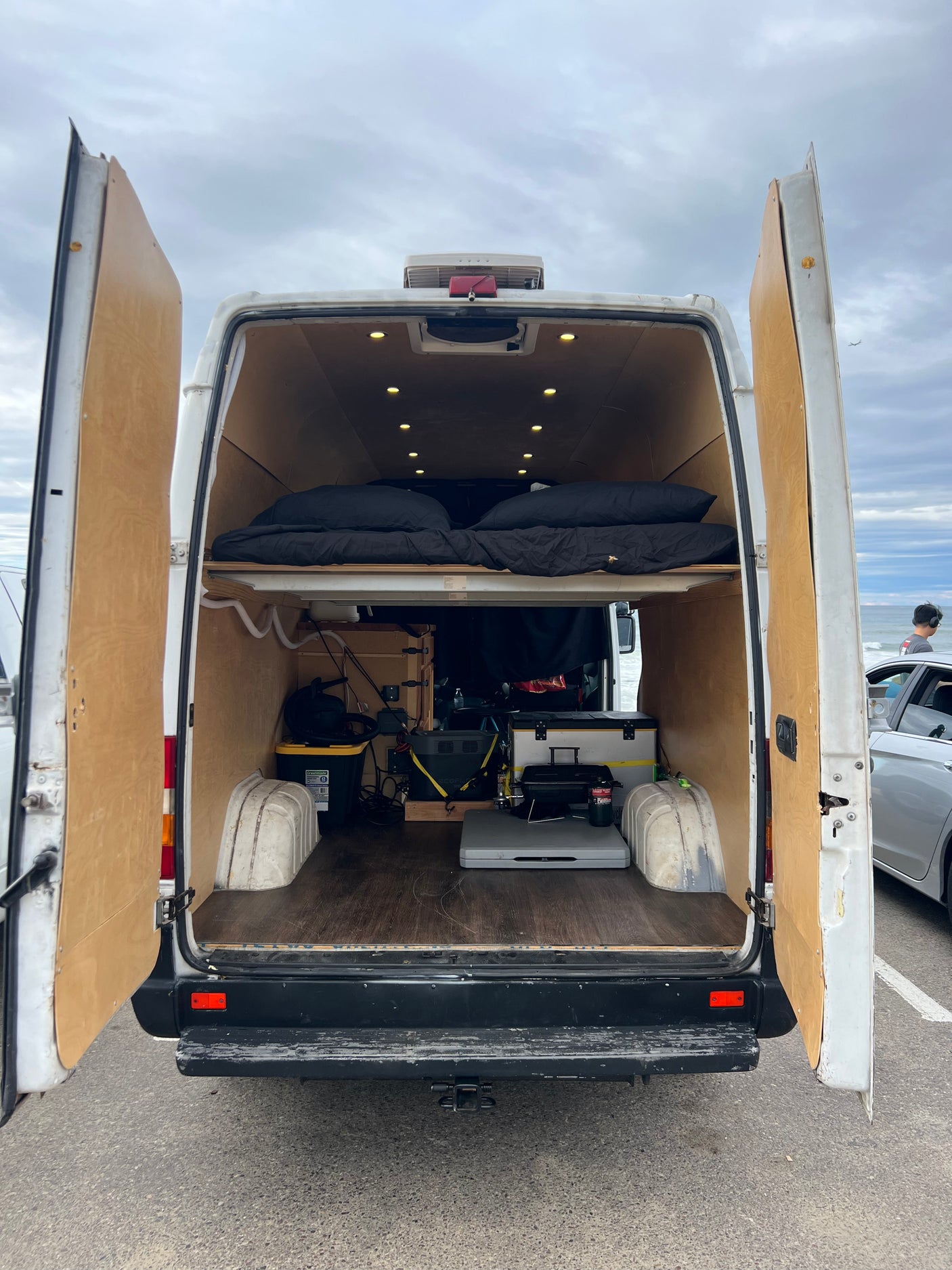 Back of a customized camper van, ready for rv rental. Reveals a comfortable elevated bed and mobile living essentials.