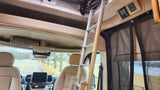 Inside an RV rental: View from the rear, showing front seats, overhead storage, ladder to bunk, and control panel. Lake seen through screen.