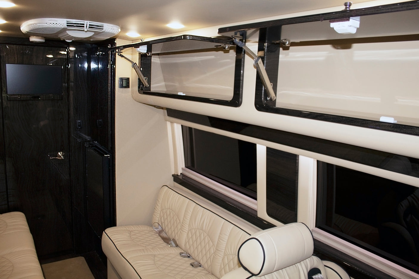 Luxury RV rental interior features cream quilted seating, dark wood trim, overhead storage, and a TV for comfortable travel.
