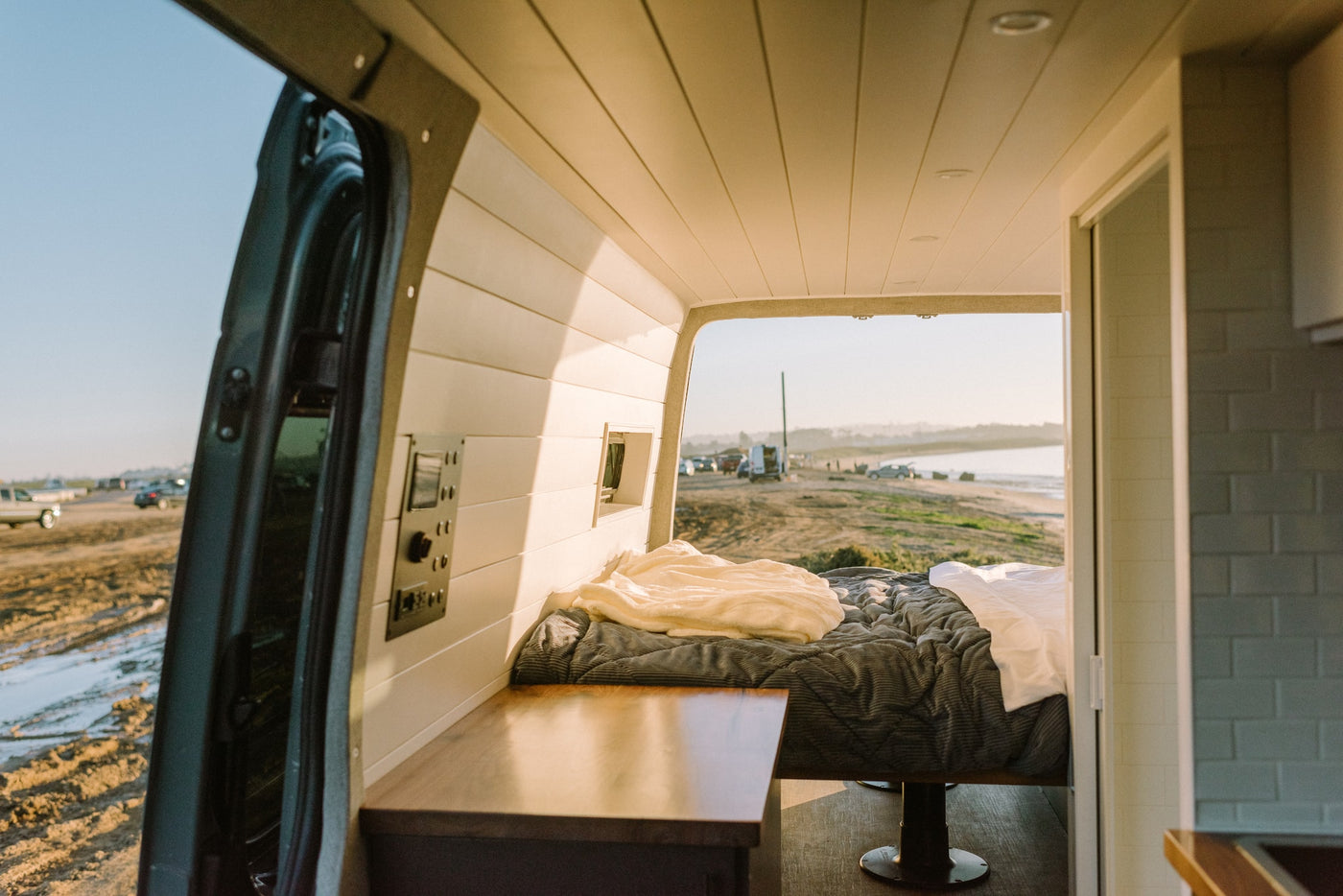 Relax in this RV rental's comfy interior, featuring a bed, wood counter, and open doors to a scenic waterside view. — photo 9