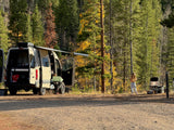 A person stands by their RV rental camper van in a vibrant fall forest campsite.