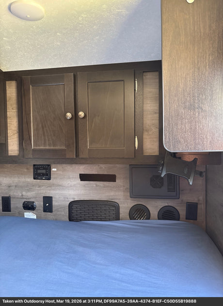 Modern RV rental sleeping area with convenient amenities: bed, cabinets, and power outlets.