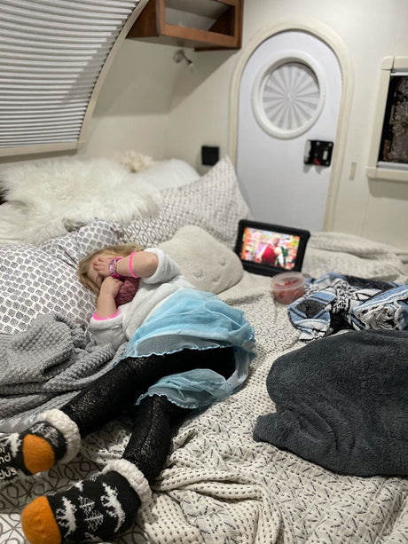 Child covers face, watching tablet on a cozy RV rental bed. Ideal for family relaxation.