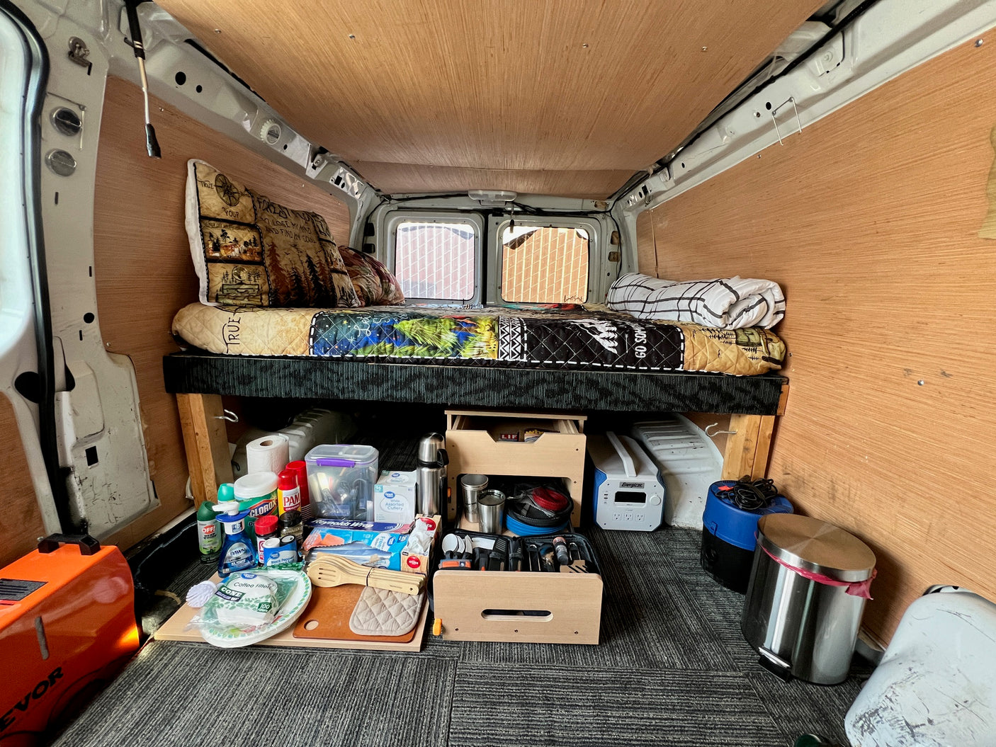 Cozy rv rental camper van interior: bed, organized kitchen supplies under it, and portable power. Ideal for road trips and camping.
