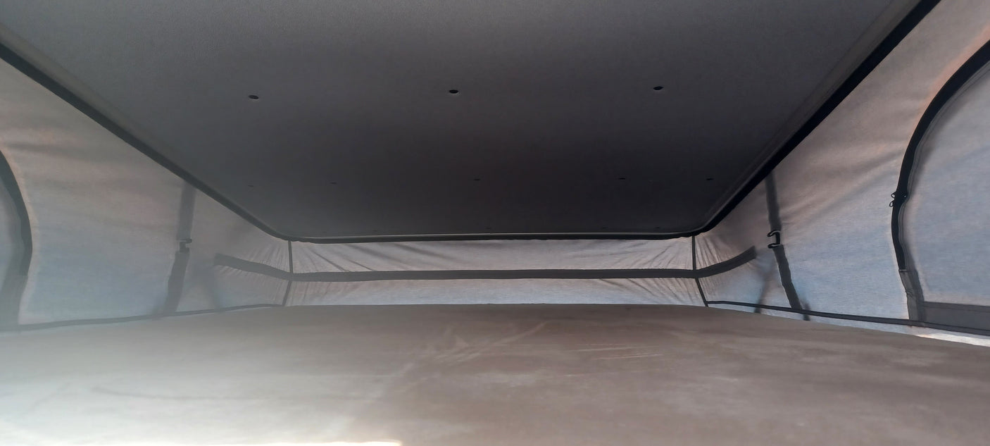 Inside an RV rental pop-top camper: spacious upper sleeping area with dark ceiling and light fabric walls.