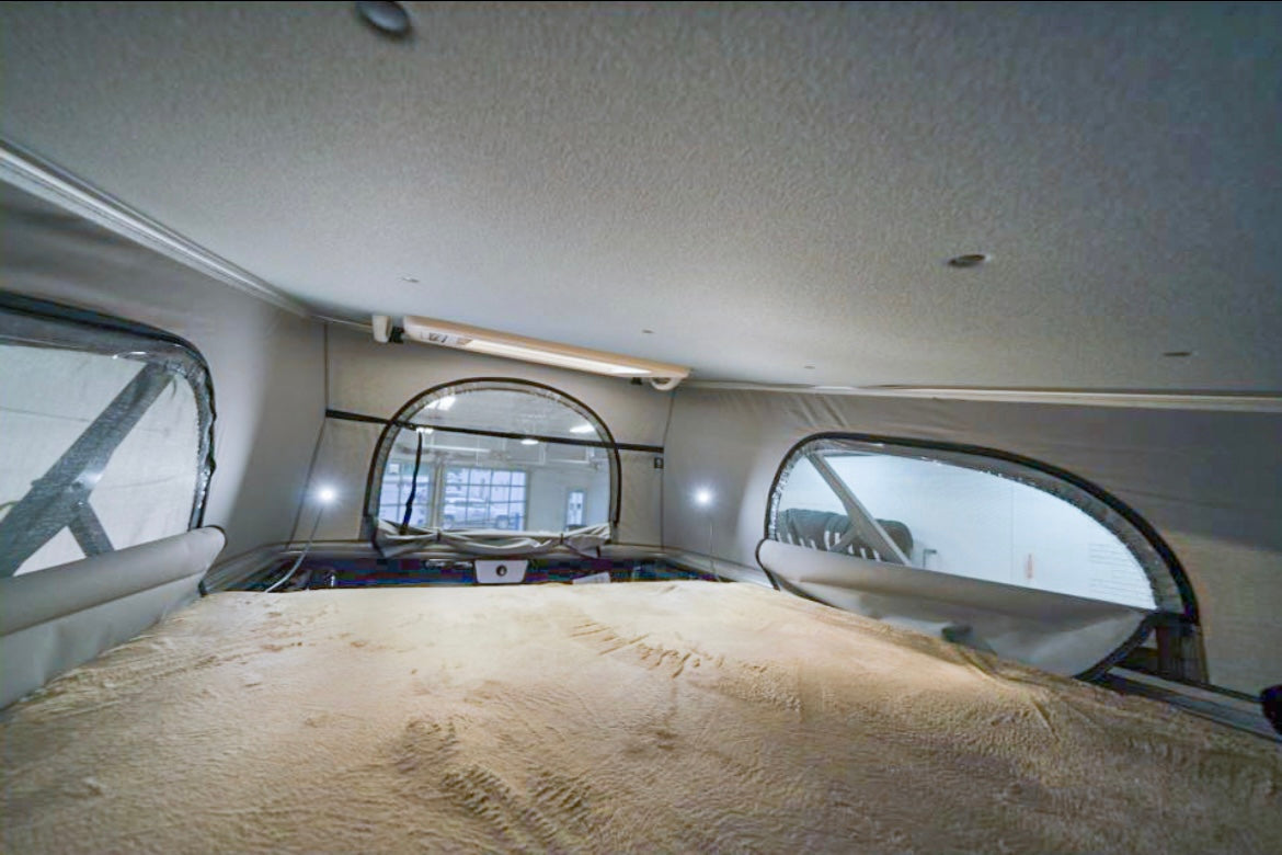 Spacious pop-top RV rental interior with a cozy bed, perfect for your next road trip adventure. Features large windows.