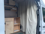 RV rental's custom camper van interior with light wood cabinetry, wall storage (basket, paper towels), and privacy curtain.