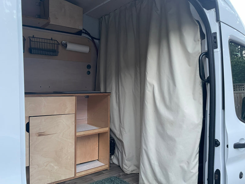 RV rental's custom camper van interior with light wood cabinetry, wall storage (basket, paper towels), and privacy curtain. — photo 11