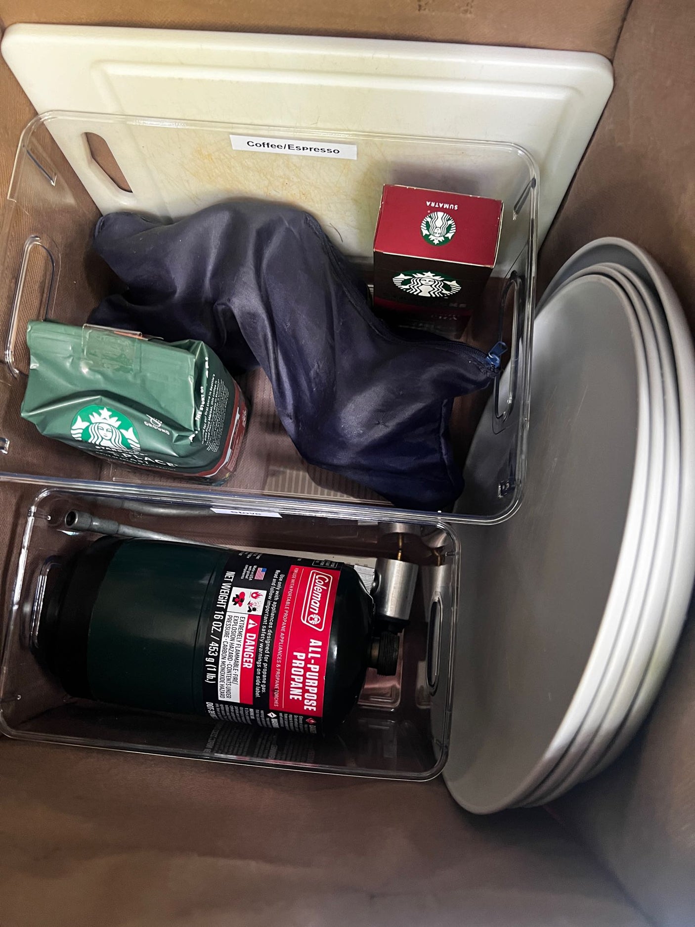 RV rental ready: organized bins with Starbucks coffee, Coleman propane, plates, and cutting board for adventures.