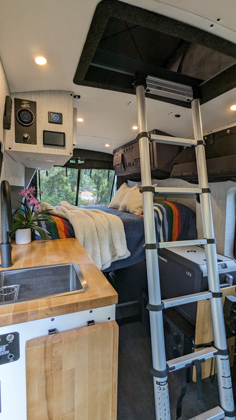 Inside a sleek rv rental: Compact kitchen, cozy bed, ladder to versatile overhead space, and Dometic cooler.