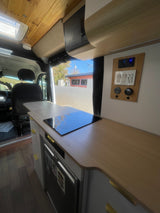 Step inside this modern RV rental! Features a compact kitchen with induction cooktop, fridge, and control panel.