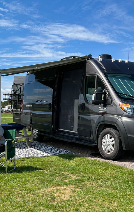 Dark gray RV rental with extended awning and open screen door, parked on grass. Ideal for a summer camping trip.