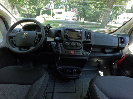 Dashboard and interior of an RV rental, offering a driver's view of the road, houses, and trees through the windshield.