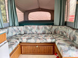 U-shaped dinette with patterned cushions and a rear bunk bed in a spacious RV rental pop-up camper interior.