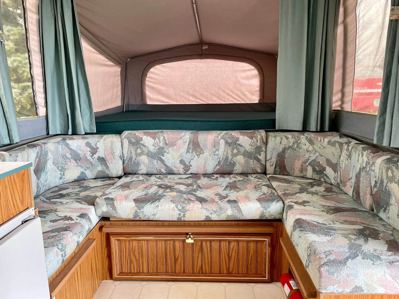 U-shaped dinette with patterned cushions and a rear bunk bed in a spacious RV rental pop-up camper interior. — photo 7