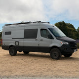 Rugged grey Mercedes Sprinter camper van with roof rack, ideal for RV rental adventures, parked on dry ground.