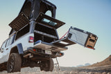 Overland-ready Jeep Gladiator with a deployed rooftop tent and slide-out fridge, perfect for RV rental adventures.