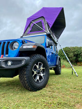 Blue Jeep Wrangler with a purple rooftop tent deployed on grass. Perfect for an RV rental camping adventure in nature.