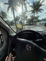 Tropical RV rental view from a Ram van driver's seat; dashboard, glare, palm trees, and caution tape visible.