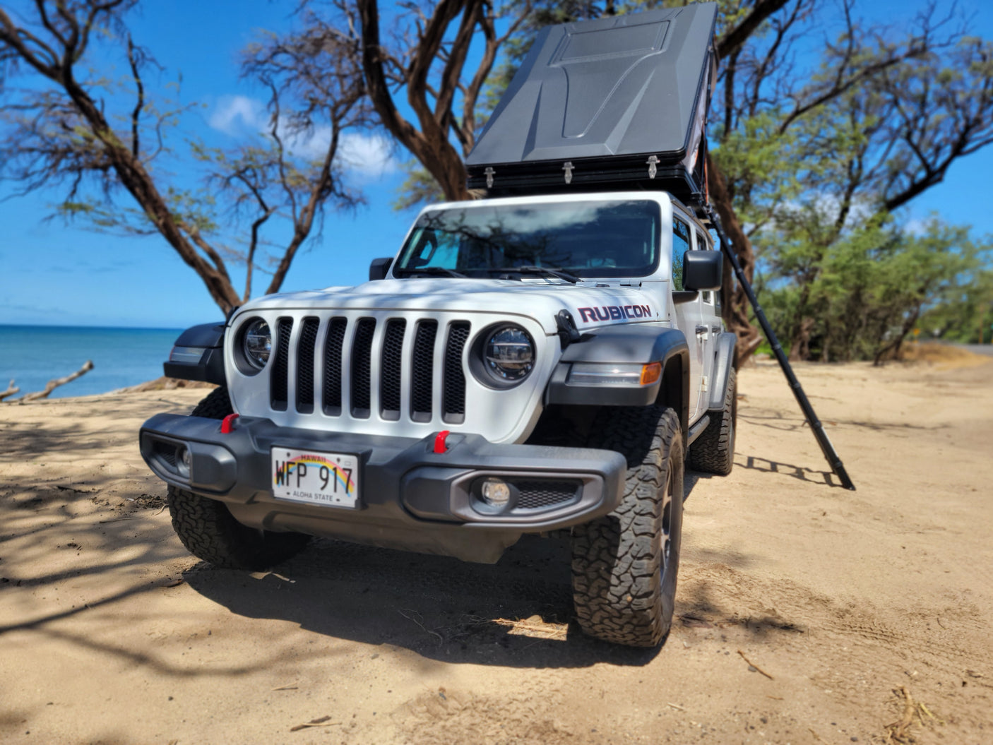 White Jeep RV rental with rooftop tent on a Hawaiian beach. Enjoy scenic overlanding & adventure camping.