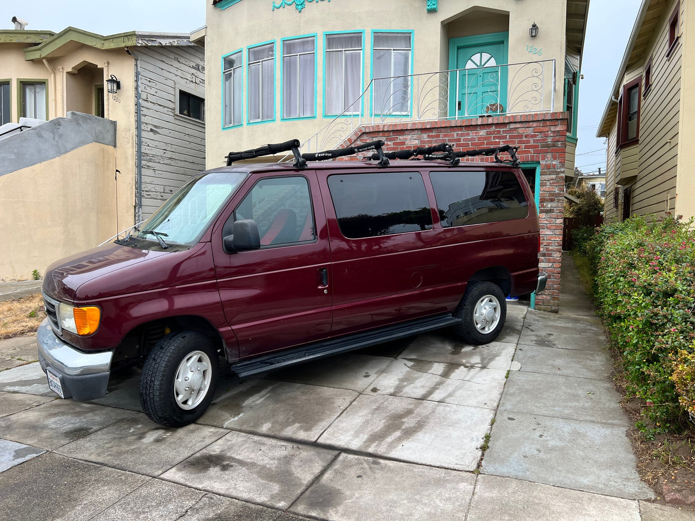 Burgundy van with surf racks, suitable as an RV rental, parked on a driveway beside residential homes. — photo 5