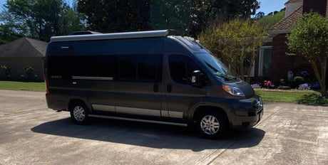 Dark grey camper van (rv rental) with an awning parked on a driveway. A house