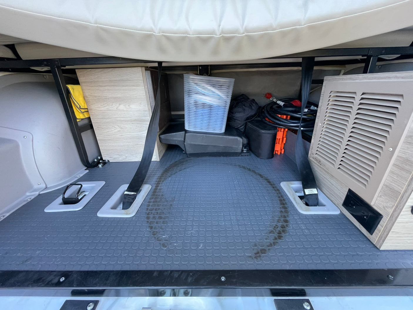 RV rental: Organized under-bed storage space with grey mat, straps, cables, and a clear bin.