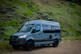 Grey Mercedes-Benz Sprinter RV, a perfect rv rental for off-road adventures, parked on a dirt path in a grassy, hilly landscape.