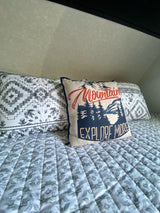 Inside an RV rental: a comfy bed with a 'Mountain Explore More' pillow and stylish geometric patterned bedding.