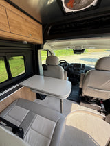 Explore this RV rental's cozy camper van interior with swivel seats, dining table, and overhead storage.