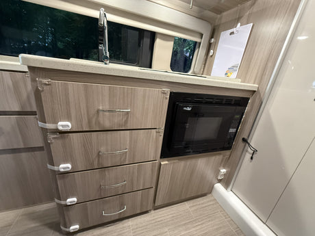This rv rental features a compact kitchen with a sink, built-in microwave, and child-safe drawers for convenience.