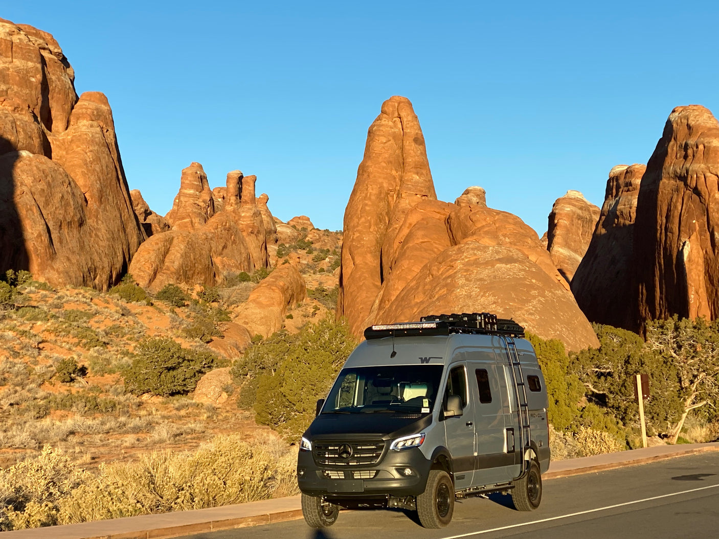 Discover a stunning desert landscape with this modern grey Sprinter van RV rental parked near towering red rocks.