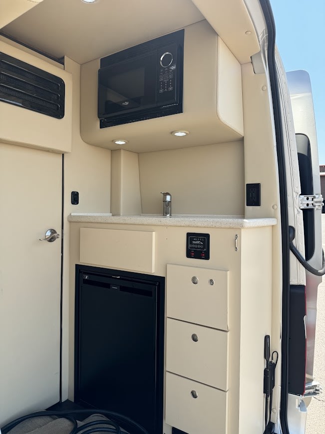 Bright **RV rental** camper van interior shows a compact kitchenette with microwave, sink, fridge, and control panel. — photo 16