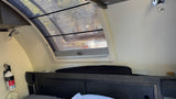 Cozy RV rental bedroom featuring a skylight with blinds, a reading light, and a mounted fire extinguisher for safety.