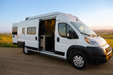 Discover adventure with this white camper van RV rental. Parked on a dirt road, its open doors reveal a cozy interior, bathed in sunset light.