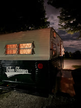 Cozy vintage 'Urban Glamper' RV rental at night, glowing warmly from within. Perfect for glamping under the cloudy sky.