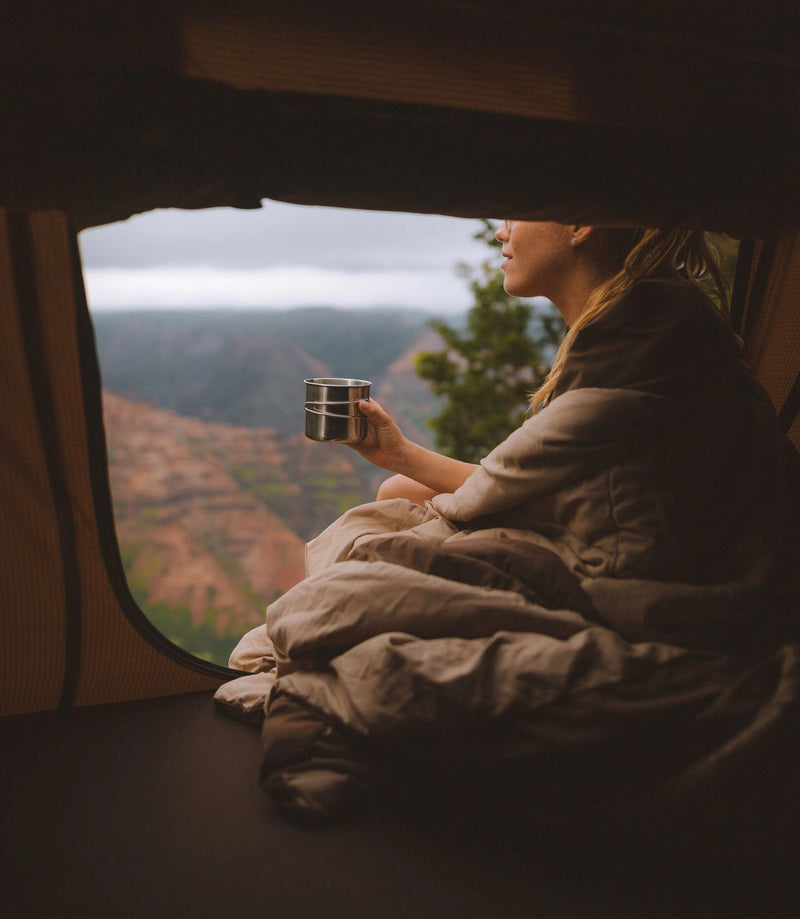 Cozy morning in an RV rental: Woman enjoying coffee with a stunning canyon view from inside, wrapped in a blanket. — photo 7