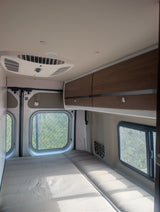 Cozy interior of an RV rental featuring a comfortable bed, windows, overhead cabinets, and an AC unit for your travels.