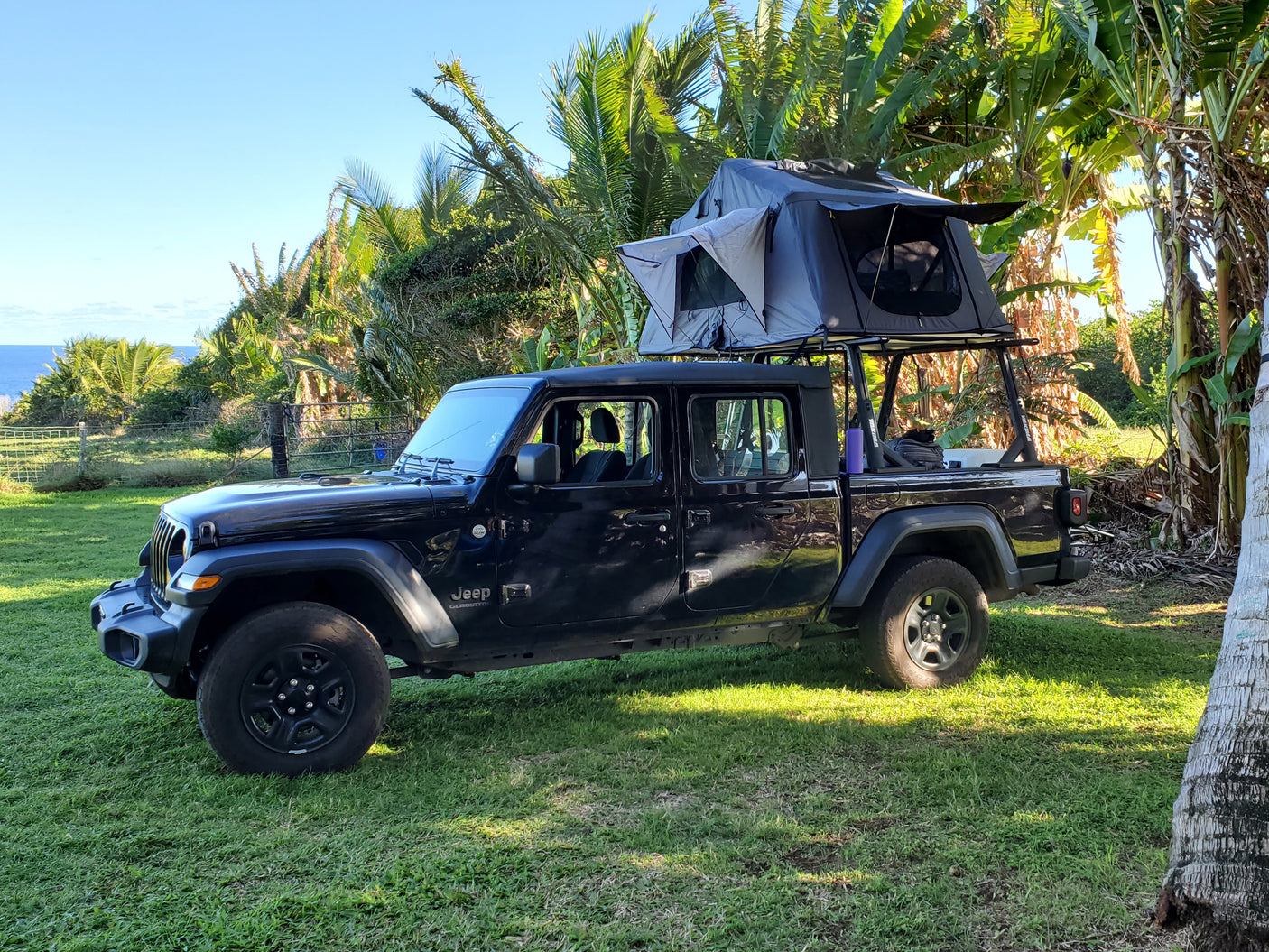 This black Jeep Gladiator truck, featuring a rooftop tent, offers a unique RV rental experience for tropical camping by the ocean.