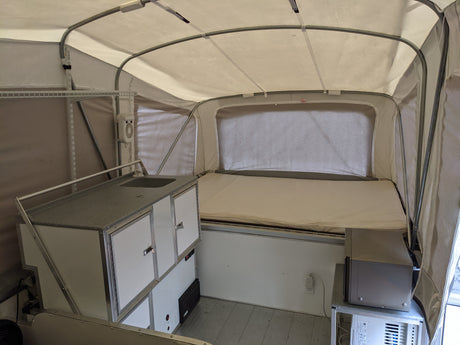 Inside an RV rental: a flexible pop-up camper setup with a sleeping area, compact kitchen, and amenities like a fan and AC.