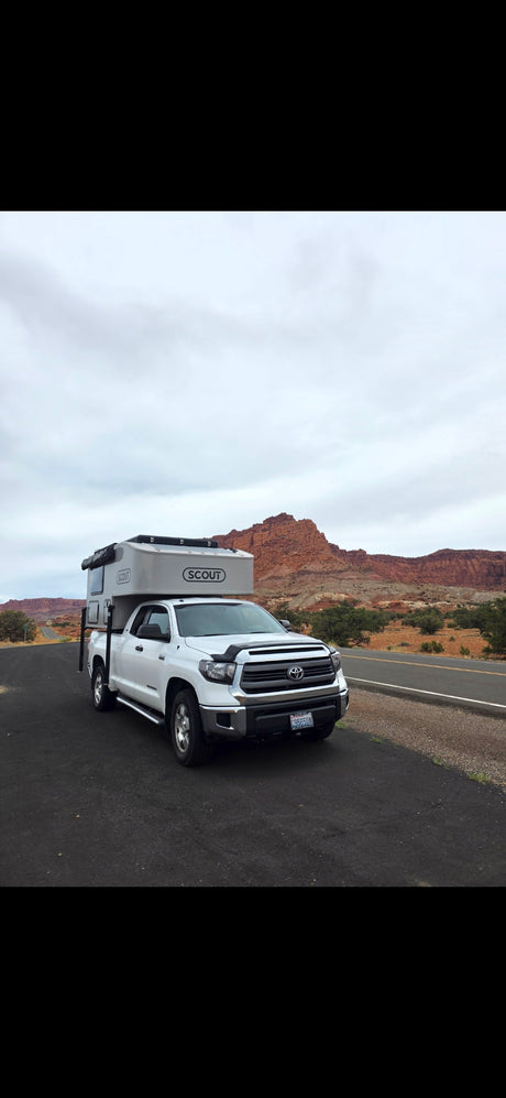 White Toyota Tundra with a "Scout" truck camper, parked by a road with red rock mountains. Perfect for your next **rv rental** adventure!