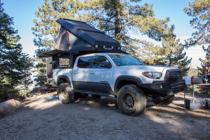 White Toyota Tacoma with an open Alu-Cab truck camper tent set up at a scenic campsite. An ideal RV rental alternative. — photo 7