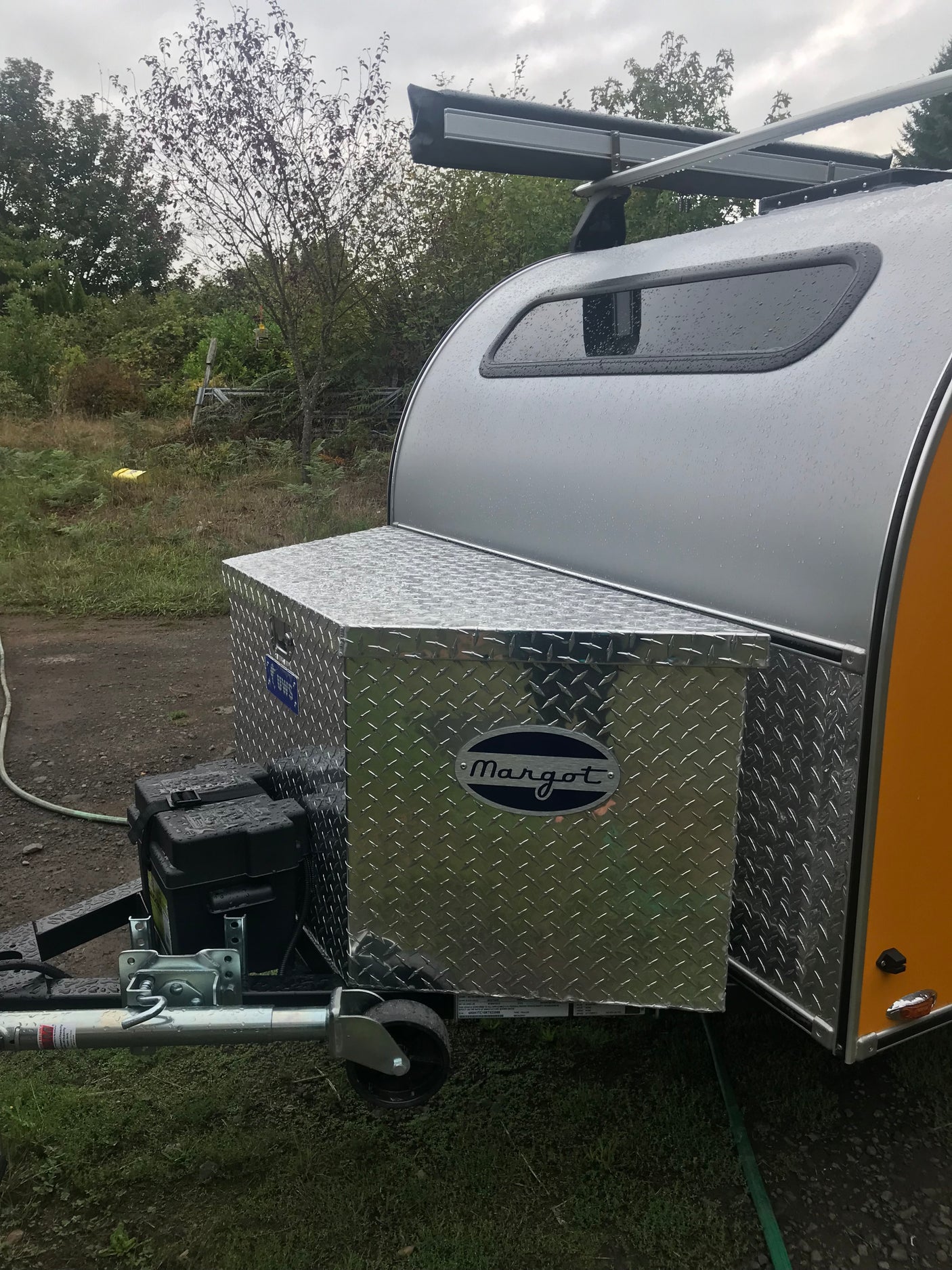 Front view of a silver teardrop camper with a diamond plate storage box, ideal for your next RV rental adventure.