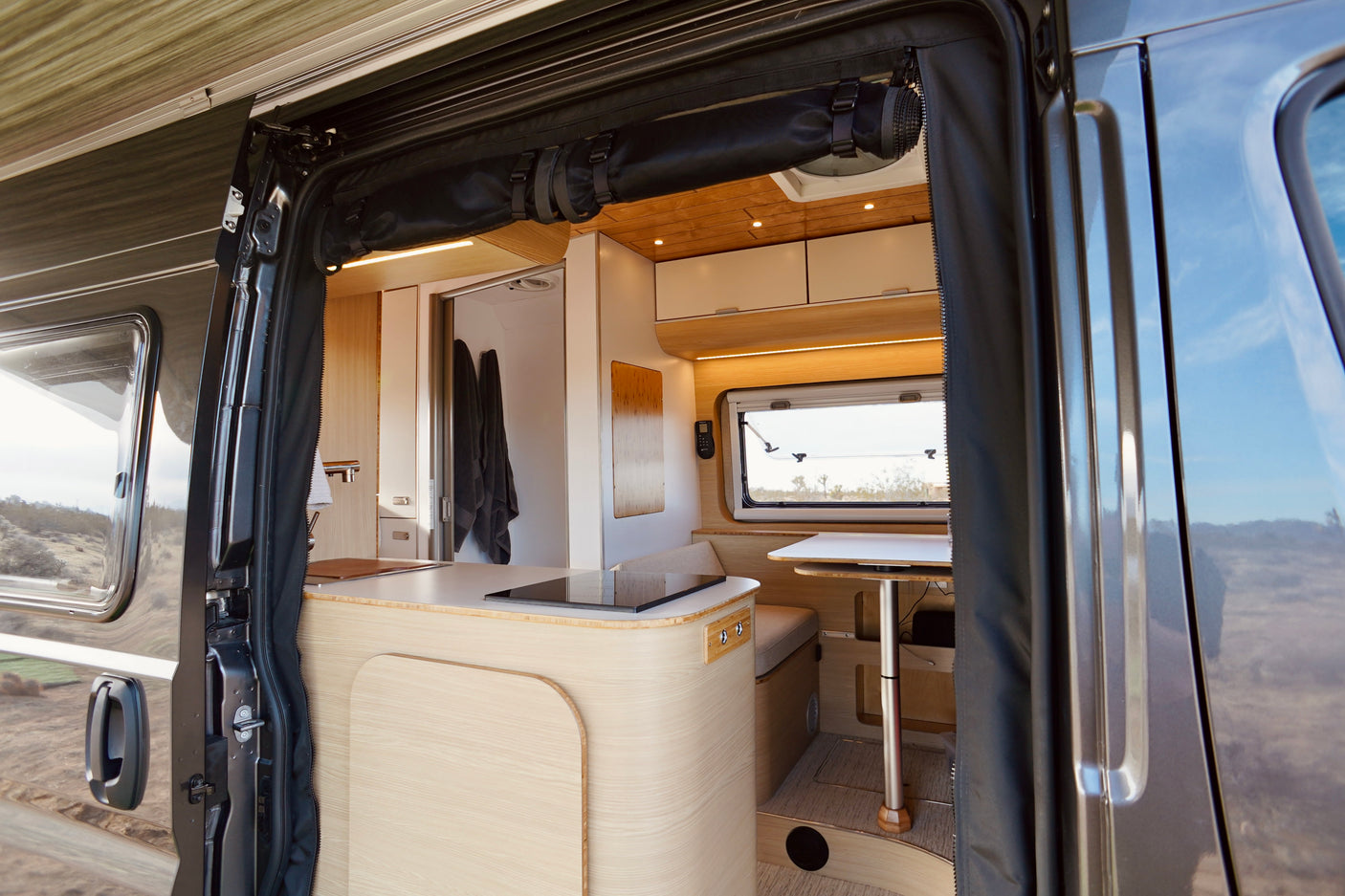 Step inside this modern campervan rv rental! View from the open door shows a spacious kitchen, dining area, and cozy interior.