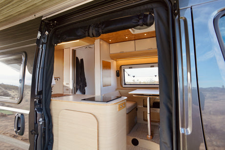 Step inside this modern campervan rv rental! View from the open door shows a spacious kitchen, dining area, and cozy interior.