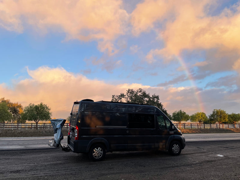 Stunning sunset sky with a rainbow over a black camper van RV rental, parked on a scenic roadside. — photo 2
